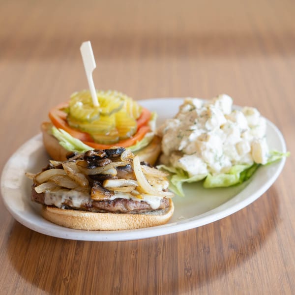 Two mini burgers, one with pickles and tomato, the other with caramelized onions and mushrooms, served with potato salad.