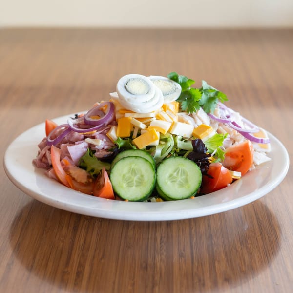 A large chef salad with ham, cheese, hard-boiled eggs, tomatoes, cucumbers, and red onion.